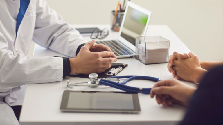 Two people talking at a desk with a stethoscope and a clipboard on it